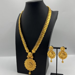 May include: A gold necklace and earrings set with a large, ornate pendant and matching earrings. The necklace is made of a chain of small, round coins.
