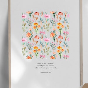 May include: A printable wall art design featuring a watercolor floral pattern with pink, orange, and yellow flowers. The text "Aspire to lead a quiet life, to mind your own business, and to work with your own hands. 1 Thessalonians 4:11" is printed below the floral pattern.