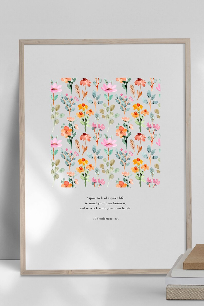 May include: A printable wall art design featuring a watercolor floral pattern with pink, orange, and yellow flowers. The text "Aspire to lead a quiet life, to mind your own business, and to work with your own hands. 1 Thessalonians 4:11" is printed below the floral pattern.