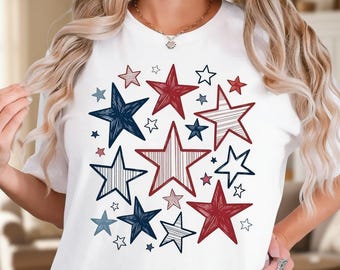 May include: A white short-sleeved t-shirt featuring a central graphic print of various stars in red, navy blue, and light blue. The stars are depicted in different sizes and styles, including solid colors, striped patterns, and sketch-like textures.
