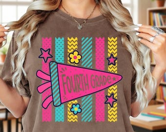 May include: A brown t-shirt featuring a graphic of a pink pennant flag with the text "FOURTH GRADE" in green. The design includes vertical stripes in teal, yellow, and pink, accented with small pink stars and colorful flower icons.