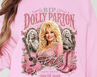 May include: A light pink crewneck sweatshirt featuring a graphic print of Dolly Parton. The design includes the text RIP DOLLY PARTON, DOLLY, LEGEND FOREVER, and COUNTRY QUEEN, alongside images of an acoustic guitar, pink cowboy boots, and roses.