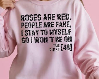 May include: A light pink sweatshirt with the text "ROSES ARE RED. PEOPLE ARE FAKE, I STAY TO MYSELF SO I WON'T BE ON THE FIRST [48]" in black. The sweatshirt is long-sleeved and the model is wearing blue denim shorts.