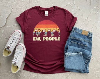 May include: A maroon t-shirt with a retro sunset graphic and five black cats. The text "EW, PEOPLE" is printed below the graphic.