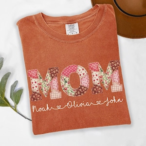 a red t-shirt with the word "MOM" printed on it, along with the names "Noah" and "Olivia" written below the letters.