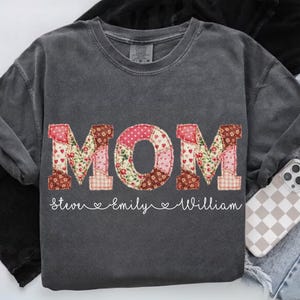 A gray t-shirt with the word "MOM" printed on it, along with the names "Stevie" and "Emilly" written below it.