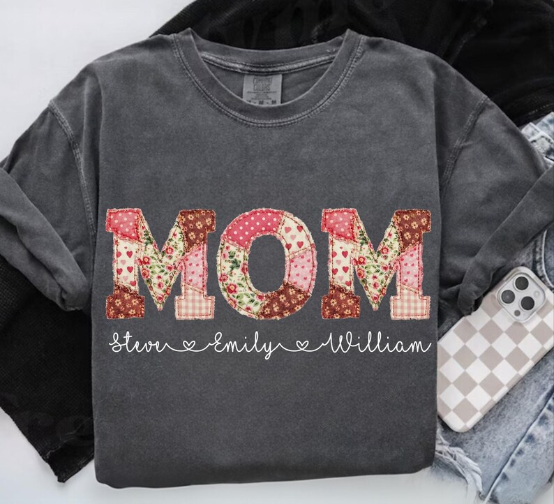 A gray t-shirt with the word "MOM" printed on it, along with the names "Stevie" and "Emilly" written below it.