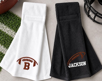 May include: A white hanging towel featuring an embroidered brown football and the letter B, alongside a black hanging towel featuring an embroidered brown football and the name JACKSON in white block lettering.
