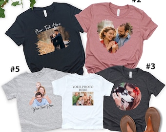 May include: Five t-shirts with different designs featuring photos. The shirts are in various colors, including gray, white, black, and pink. The designs include a couple in a heart shape, a dog, a family photo, and a couple in a forest.