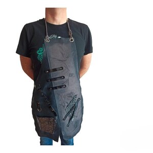 May include: A black apron with a distressed look and a pocket. The apron has a black leather strap and a silver buckle.