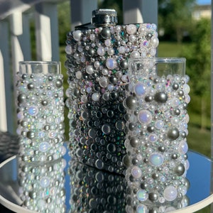 May include: A set of three silver flasks decorated with iridescent white and gray pearls. The flasks are made of metal and have a shiny finish.