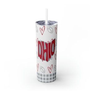 May include: White tumbler with a red and gray "OHIO" design in the shape of the state of Ohio. The tumbler is decorated with a pattern of gray hearts and footballs. The bottom of the tumbler has a gray and white checkered pattern.