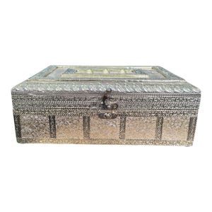 May include: An ornate, gold-coloured rectangular box with detailed embossed patterns and a hinged lid. The box has a decorative clasp and is likely for storing jewellery or small keepsakes. The box is approximately 25 cm long.