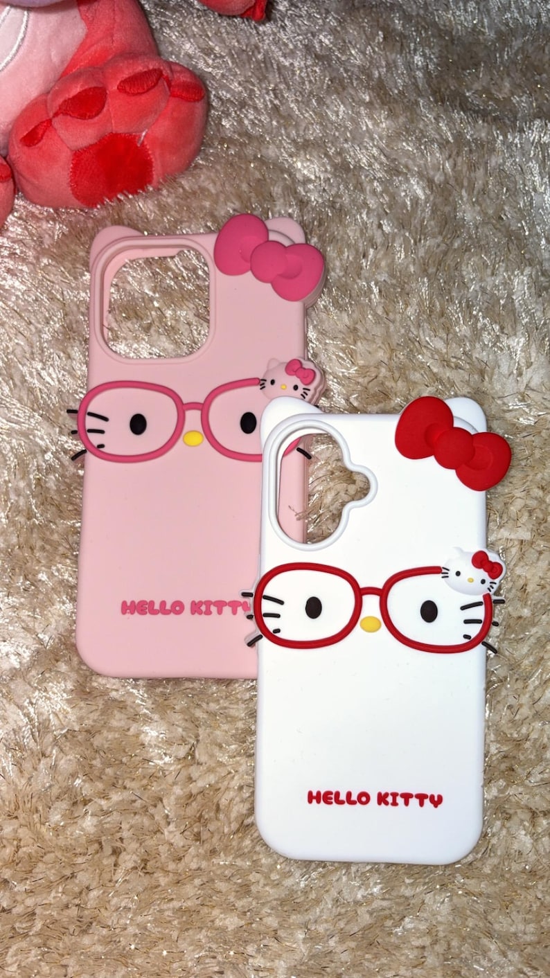 May include: Two phone cases featuring Hello Kitty designs. One is pink with a pink bow and glasses, the other is white with a red bow and glasses. Both cases have the words "Hello Kitty" printed on them.