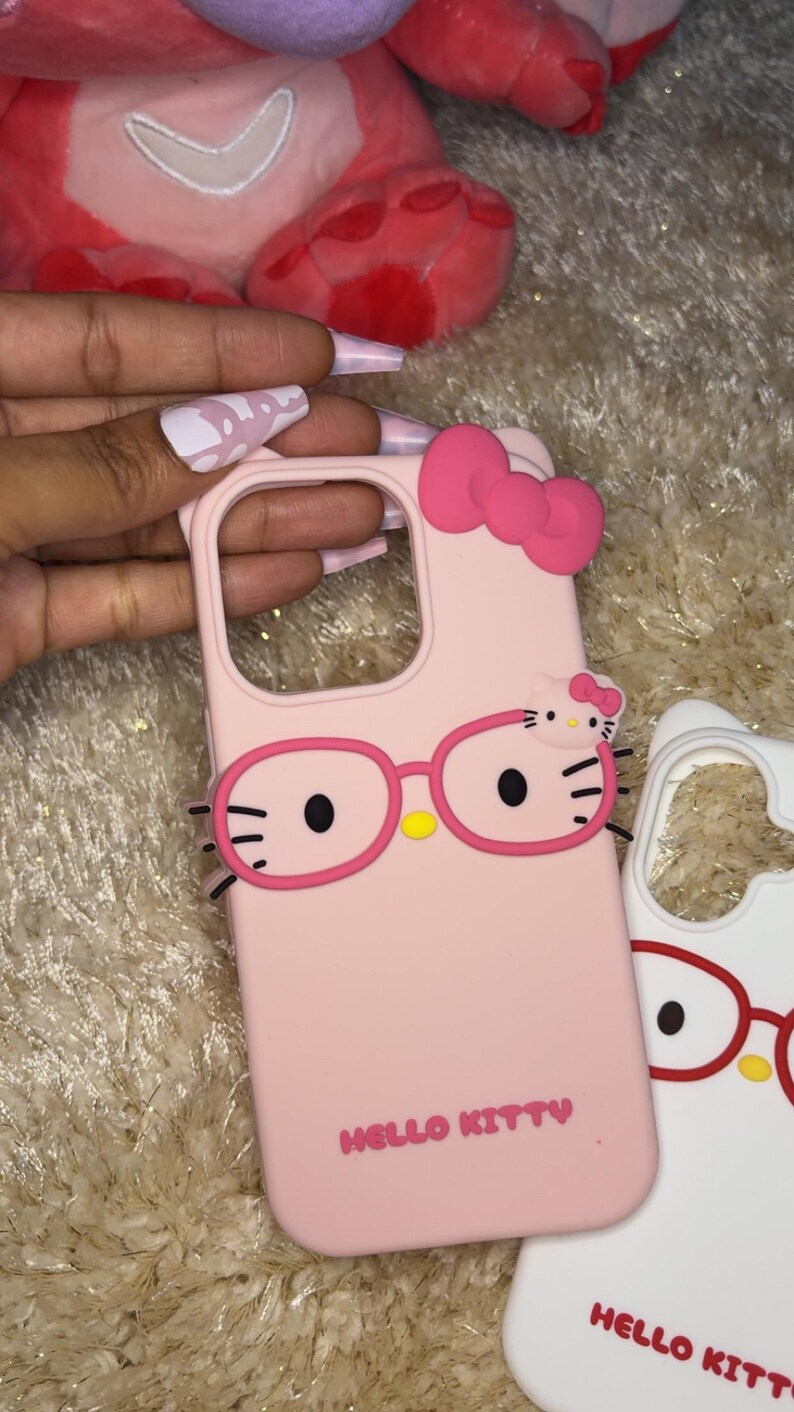 May include: Pink phone case featuring a Hello Kitty design with glasses and a bow. The case has the words "HELLO KITTY" printed on it. A second white phone case with a similar design is also visible.