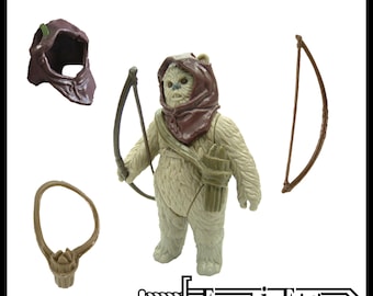May include: Replacement accessories for Warok the Ewok action figure, including a brown hood, a brown bow, and a brown quiver with strap. The set features a cream-coloured Ewok figure wearing a brown hood, holding a bow, and carrying a quiver.