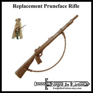 May include: A brown plastic rifle with a strap. The rifle has a black plastic grip and a brown plastic barrel. The rifle is a replacement part for a vintage action figure.