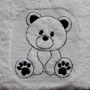 May include: A white embroidered teddy bear with black outlines and paw prints. The bear is sitting with its legs crossed and has a simple, friendly expression.