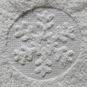 以下が含まれることがあります： 刺繍された雪の結晶のデザインが施された白いバスタオルです。