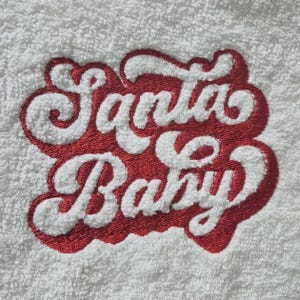 May include: White towel with red embroidered text that says "Santa Baby" in a retro font.