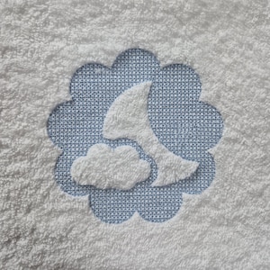 May include: White terry cloth towel with a blue floral design in the center. The design features a white crescent moon and cloud against a blue background. The towel has a soft, textured appearance.