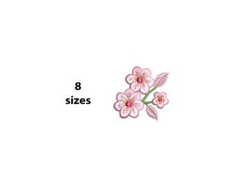 May include: Embroidered floral design featuring three pink flowers with yellow centers and green stems. The design includes two leaves and the text "8 sizes" in black. The flowers have a delicate, detailed appearance.