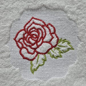Può includere: Rosa rossa ricamata con foglie verdi su un asciugamano bianco.