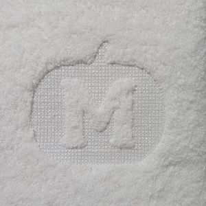 May include: White fluffy towel with a white pumpkin shape embroidered with the letter "M" in the centre.