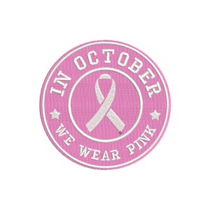 Pode incluir: Um patch bordado rosa com o texto "IN OCTOBER WE WEAR PINK" circundando uma fita branca. O patch tem um design circular com costura branca e detalhes de estrela, perfeito para roupas.
