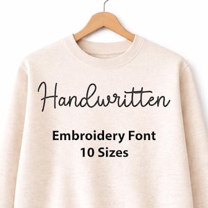 May include: Cream-colored sweatshirt with the word "Handwritten" in black script. Below, the text reads "Embroidery Font 10 Sizes". The sweatshirt hangs on a wooden hanger.