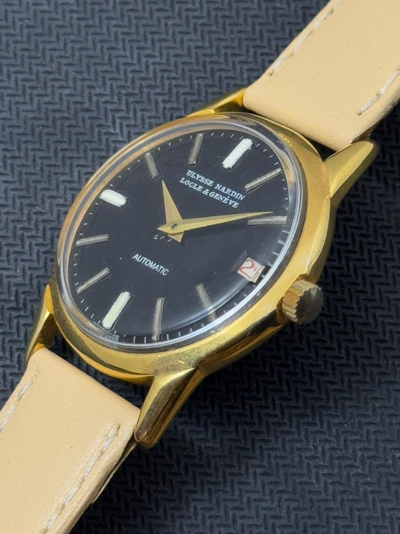 May include: A gold-tone wristwatch with a black face and white markings. The watch face reads "ULYSSE NARDIN LOCLE & GENEVE" and "AUTOMATIC".