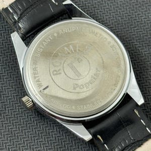 K&ouml;nnte beinhalten: Nahaufnahme der R&uuml;ckseite einer silbernen Uhr mit einem schwarzen Lederarmband. Das Zifferblatt der Uhr tr&auml;gt die Aufschrift "Roamer" und "Popular". Die R&uuml;ckseite der Uhr tr&auml;gt die Aufschrift "Water-Resistant Anuplastic etc. 0.5 ATM Swiss Made Steel Back Stainless."