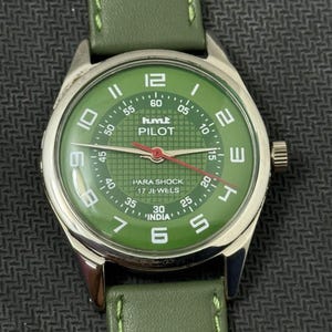 Pode incluir: Um rel&oacute;gio de pulso verde com caixa prateada e pulseira de couro verde. O mostrador do rel&oacute;gio &eacute; verde com algarismos e ponteiros brancos, e o texto "PILOT" e "INDIA" s&atilde;o vis&iacute;veis.