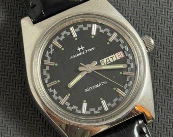 Hamilton Automatic. Kolor tarczy z datą i dniem tygodnia. Czarny mechanizm zegarka męskiego. Autentyczny mechanizm ETA.