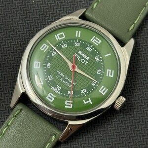 Pode incluir: Um rel&oacute;gio de pulso vintage com mostrador verde e caixa prateada. O mostrador exibe algarismos brancos e o texto "hmt PILOT". Possui uma pulseira de couro verde. Os ponteiros do rel&oacute;gio s&atilde;o vermelhos.