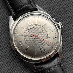May include: A silver wristwatch with a black leather strap. The watch face has large silver numerals at 12, 3, 6, and 9 o'clock, a textured centre, and a red second hand. The watch is labelled "Pilot" and "Para Shock 17 Jewels".
