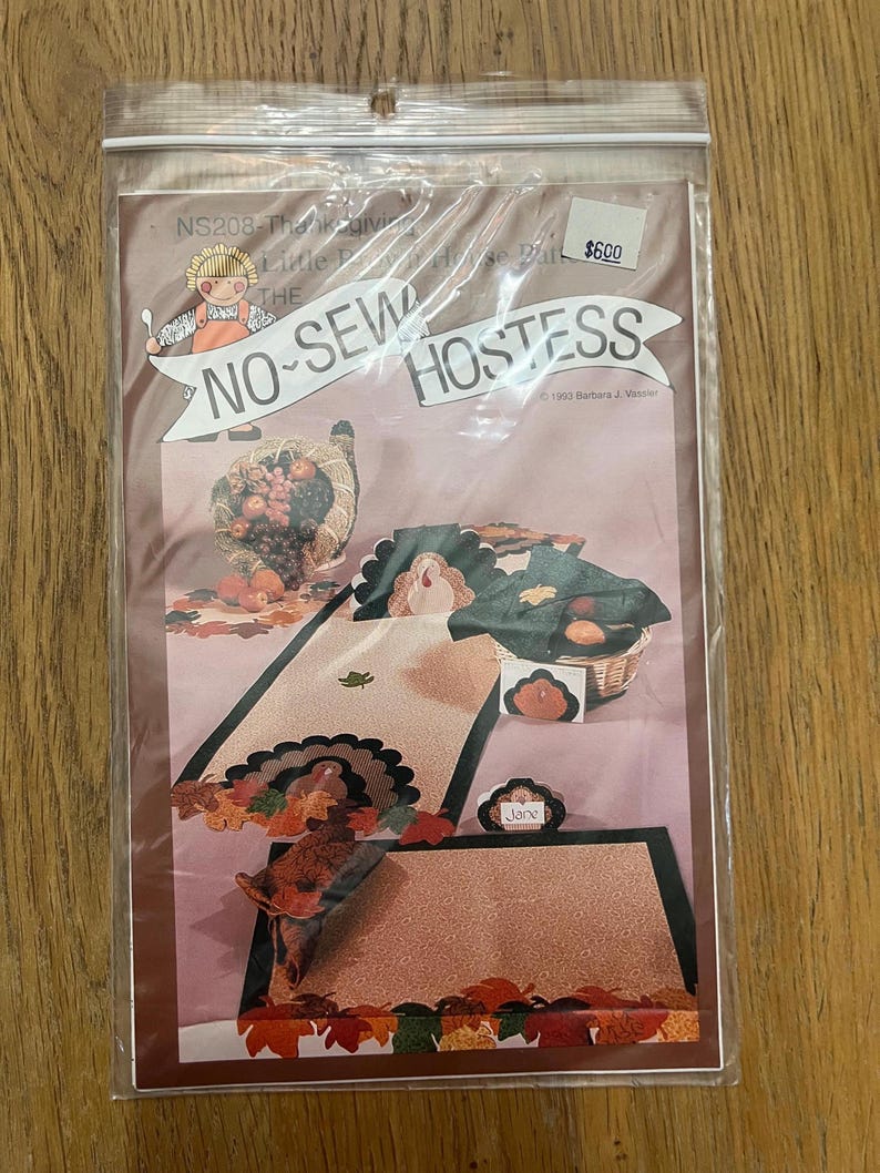 K&ouml;nnte beinhalten: Ein Bastelset zum Thema Thanksgiving in Braun-, Beige- und Gr&uuml;nt&ouml;nen. Das Set enth&auml;lt einen Truthahn, Bl&auml;tter und eine Platzkarte. Der Text auf der Verpackung lautet "No-Sew Hostess" und "6,00 &euro;".