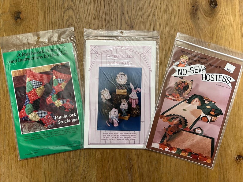 K&ouml;nnte beinhalten: Drei Bastelvorlagen zum N&auml;hen einer Patchwork-Socke, eines Bauernhof-T&uuml;rh&auml;ngers und eines No-Sew-Hostess-Teppichs. Die Vorlagen sind auf wei&szlig;em Papier mit bunten Illustrationen gedruckt.