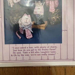 K&ouml;nnte beinhalten: Ein Set aus f&uuml;nf handgefertigten Stofftieren, darunter eine Katze, ein Pferd, ein Schwein und zwei Kaninchen. Die Spielzeuge sind alle aus rosa und wei&szlig;en Stoffen mit gestickten Details. Die Spielzeuge sind auf einer Holzbasis mit einem Zitat &uuml;ber einen lustigen Bauernhof angeordnet.