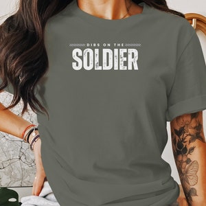 May include: A green t-shirt with the text "DIBS ON THE SOLDIER" printed in white on the front.