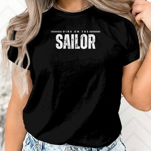 May include: Black t-shirt with white text that reads "Dibs on the Sailor".