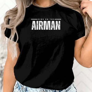 May include: Black t-shirt with white text that reads "Dibs on the Airman".