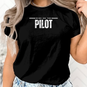 May include: Black t-shirt with white text that reads "Dibs on the Pilot"
