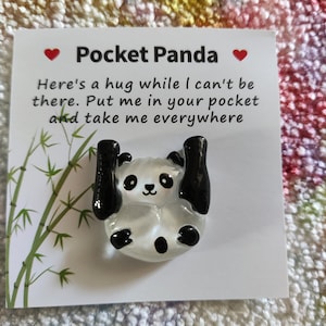 Op de afbeelding: Een witte glazen panda-bedel met zwarte oren, ogen en poten. De bedel bevindt zich op een witte kaart met de tekst "Pocket Panda" en "Here's a hug while I can't be there. Put me in your pocket and take me everywhere."