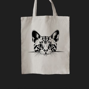 Pu&ograve; includere: Una borsa tote bianca con un'illustrazione in bianco e nero di un viso di gatto che sporge dalla parte superiore.