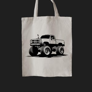 May include: A white tote bag with a black silhouette of a monster truck. The truck has large tires and a raised suspension.