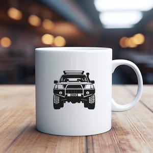 May include: White ceramic mug with a black silhouette of a 4x4 vehicle with a roof rack. The vehicle is facing the viewer.