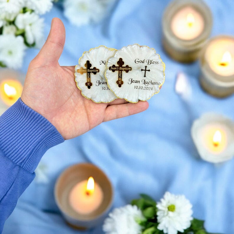 May include: Two white round favours with gold trim and a gold cross design. The favours have the text "God Bless Jean Luciano 10.10.2024" and "Jean's Baptism 10.10.2024".