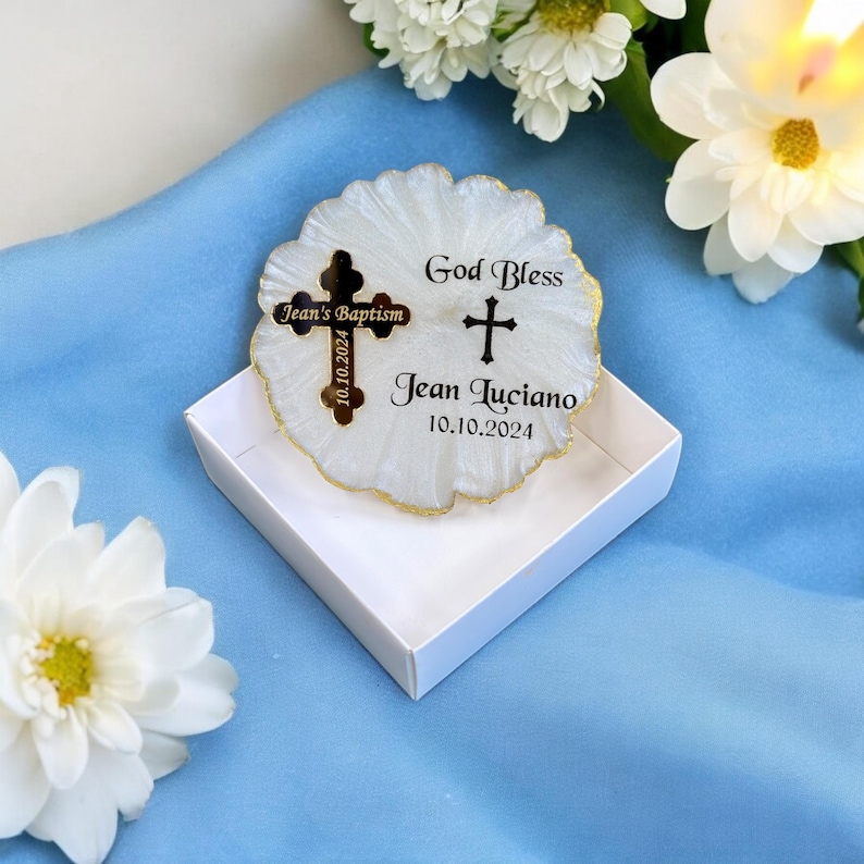 May include: White circular favour with a gold trim and two gold crosses. The larger cross has the text "Jean's Baptism 10.10.2024" and the smaller cross has the text "God Bless Jean Luciano 10.10.2024".