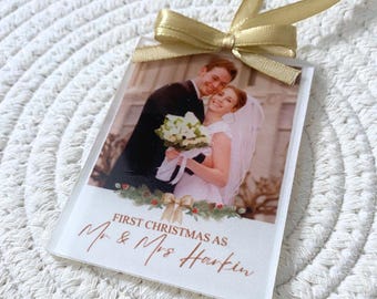 Puede incluir: Adorno navideño rectangular transparente con una foto de boda de una pareja sonriente. El adorno tiene una cinta y un lazo dorados. El texto dice "First Christmas as Mr & Mrs Harkin" en color cobre.